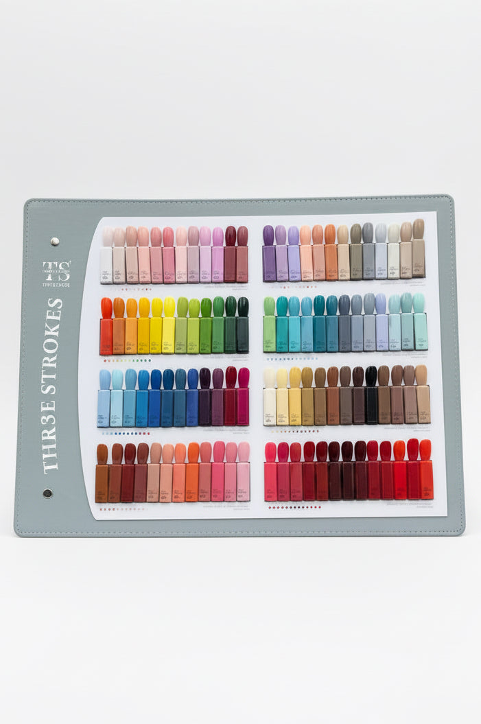 A hand holds a large Three Strokes nail color swatch book in front of a building exterior. The book displays many rows of small nail polish color samples in a wide range of shades, including pinks, purples, greens, blues, browns, and reds.