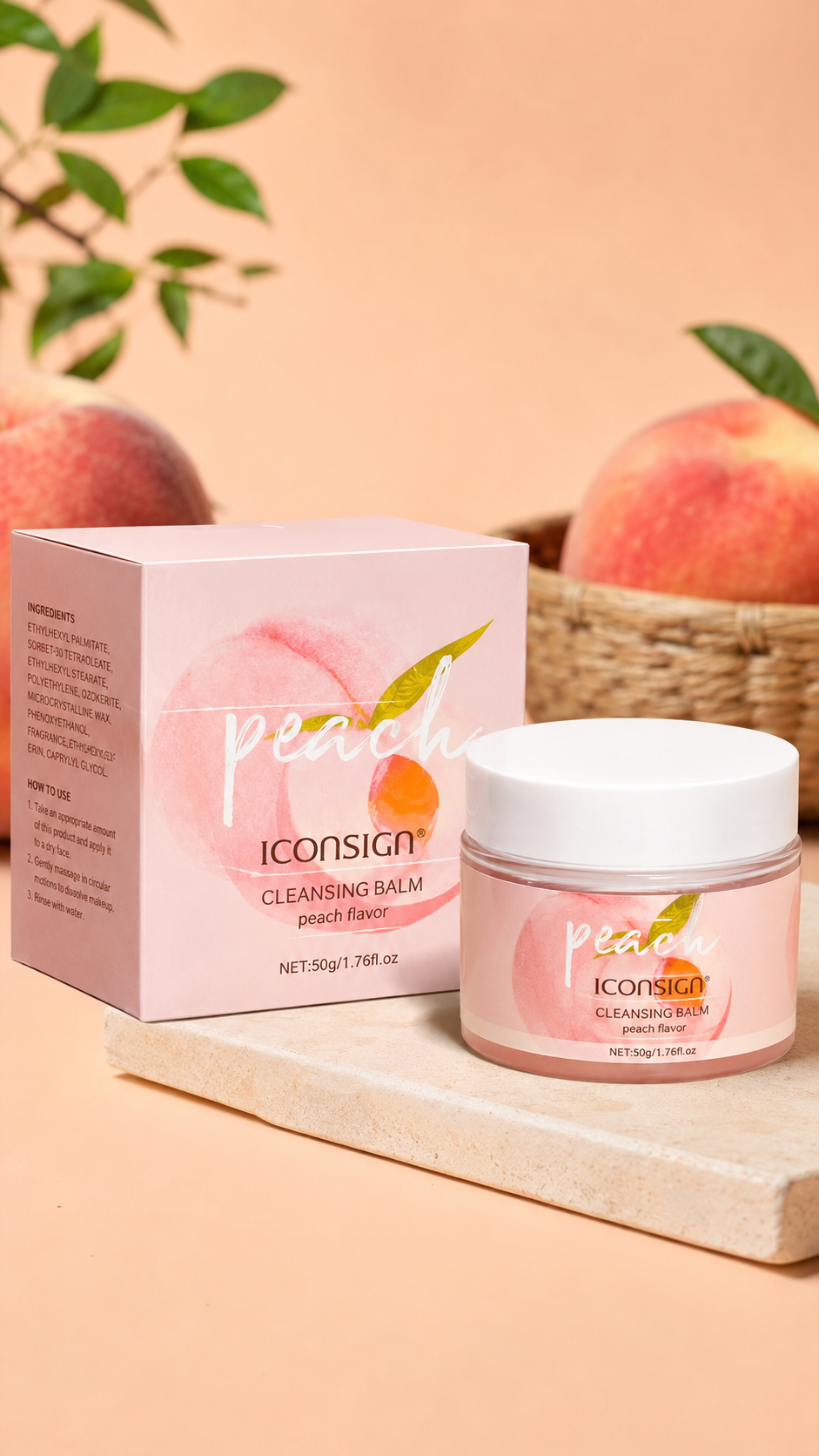 A jar of Iconsign Cleansing Balm in peach flavor sits next to its pink packaging box on a light stone slab, with peaches and green leaves blurred in the background against a peach-colored backdrop.