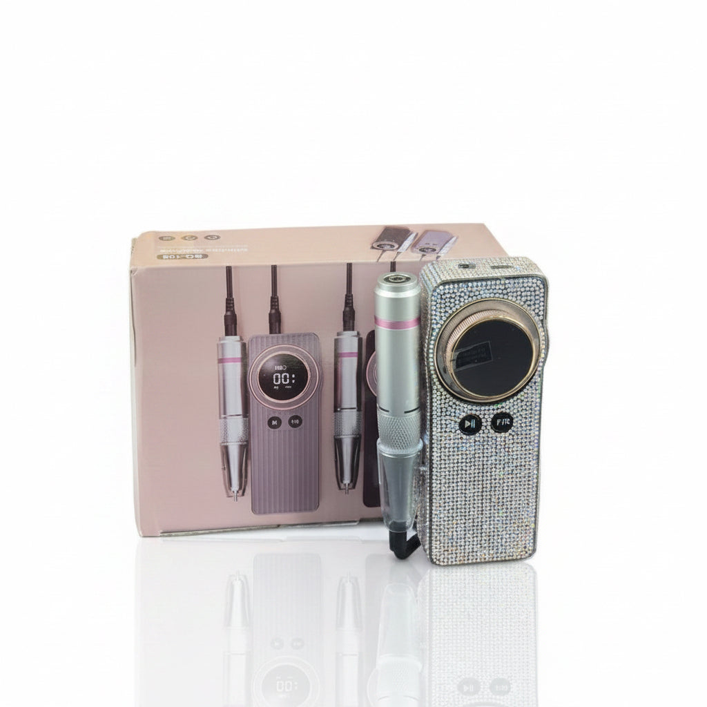 A handheld beauty device set displayed with its retail box on a white pedestal. The set includes a silver and pink electronic pen, a matching digital control pad, and a rhinestone-covered rectangular device with a circular display window.