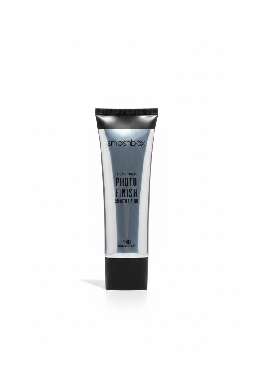 A tube of Smashbox Photo Finish Primer stands on a glass display counter in a retail store. The silver tube with black caps is centered in front of a laptop, with shelves of other products visible in the background.