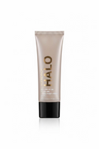A tube of Halo Healthy Glow All-In-One Tinted Moisturizer SPF 30 standing on a glass display counter inside a retail store. The packaging is metallic silver with a black cap, and the background shows shelves filled with other cosmetics.