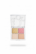 A hand holding an open Dior 4-pan eyeshadow palette. The clear plastic case features a large silver-tone Dior logo on the inside of the lid, and the four eyeshadow pans are arranged in a grid with gold, pink, champagne, and peach tones, all embossed with the Dior Oblique pattern.