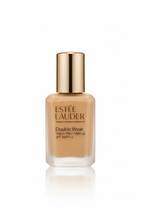 Estée Lauder Double Wear Stay-in-Place Makeup SPF 10+ PA++ liquid foundation in a frosted glass bottle with a metallic gold cap, displayed on a glass surface with its blue box in the background.