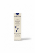 A person holds a box of EMBRYOLISSE Lait-Crème Concentre Multi-functions moisturizer in a retail store setting with a glass display counter and shelves in the background.