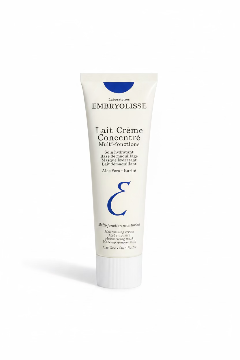 A hand holding a white tube of Embryolisse Lait-Crème Concentré Multi-fonctions moisturizer cream, with a person's legs and jeans visible in the background.