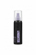 A black cylindrical hair product bottle labeled 'ALL NIGHTGLITTER' with a silver spray top, standing on a glass counter in a retail store. A laptop, packaging boxes, and a person's hand are visible in the background.