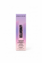 A box of Urban Decay All Nighter Makeup Setting Spray standing on a glass display counter in a retail store. The packaging is a soft pink-to-lavender gradient with bold black text.