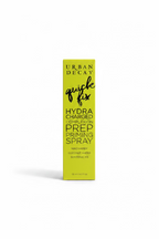 A yellow box of Urban Decay Quick Fix Hydra Charged Prep Priming Spray stands on a glass display counter in a retail store. Winston and Mynk boxes are visible in the background, along with a laptop and other cosmetics.