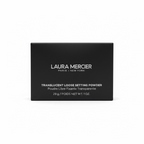 A black Laura Mercier box of Translucent Loose Setting Powder placed on a glass shelf, with a laptop and other cosmetic items in the background.