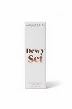 A white box of Anastasia Beverly Hills Dewy Set Setting Spray standing on a glass display counter in a retail store. The box features the brand name 'ANASTASIA BEVERLY HILLS' and the product name 'Dewy Set' in brown lettering.