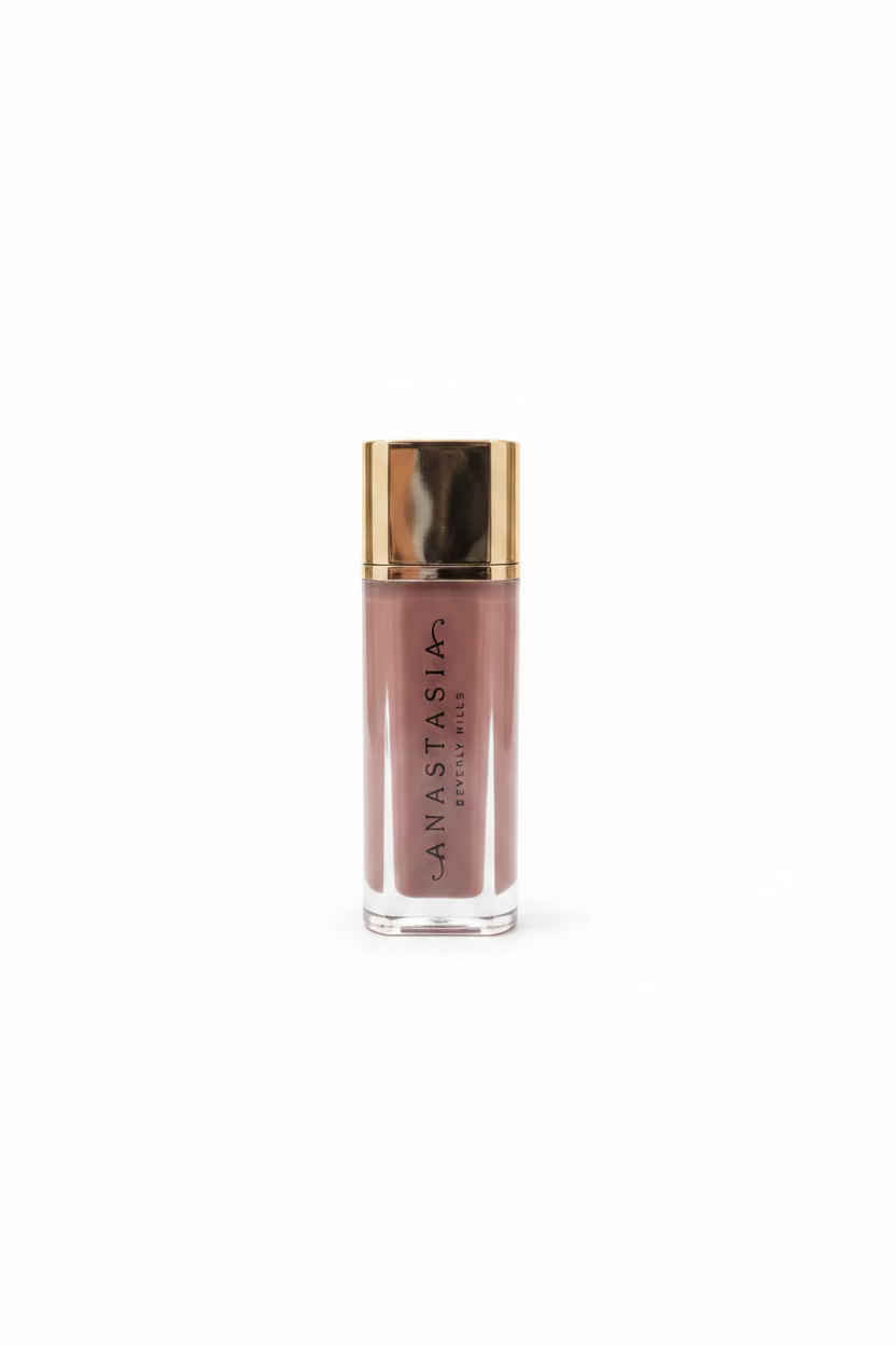 Anastasia Beverly Hills Liquid Blush in a clear rectangular bottle with a metallic gold cap, displayed on a glass shelf next to a silver Apple laptop.