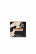 Fenty Beauty Sun Streaks matte powder foundation in a black and white textured box, placed on a glass table with a laptop and other boxes in the background.
