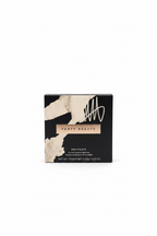 Fenty Beauty Sun Streaks matte powder foundation in a black and white textured box, placed on a glass table with a laptop and other boxes in the background.
