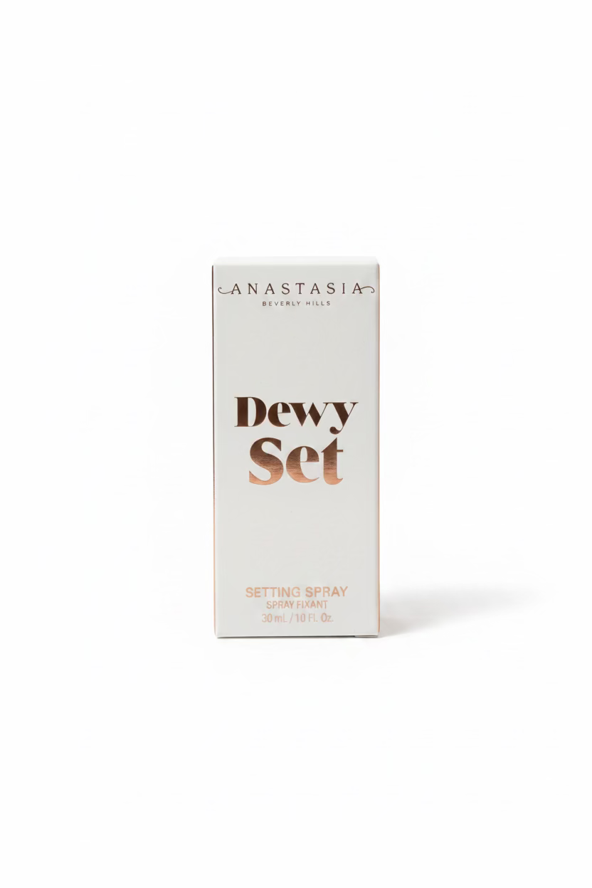 A white box of Anastasia Beverly Hills Dewy Set Setting Spray standing on a glass table, with a laptop and store items blurred in the background.