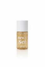 A bottle of Anastasia Beverly Hills Dewy Set Setting Spray with a white pump and a gold glitter bottle, sitting on a glass shelf in front of a laptop.
