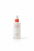 A white bottle of Peach & Lily Glass Skin Veil Mist with a coral-red pump cap, displayed on a glass shelf in front of Medcube skincare boxes.