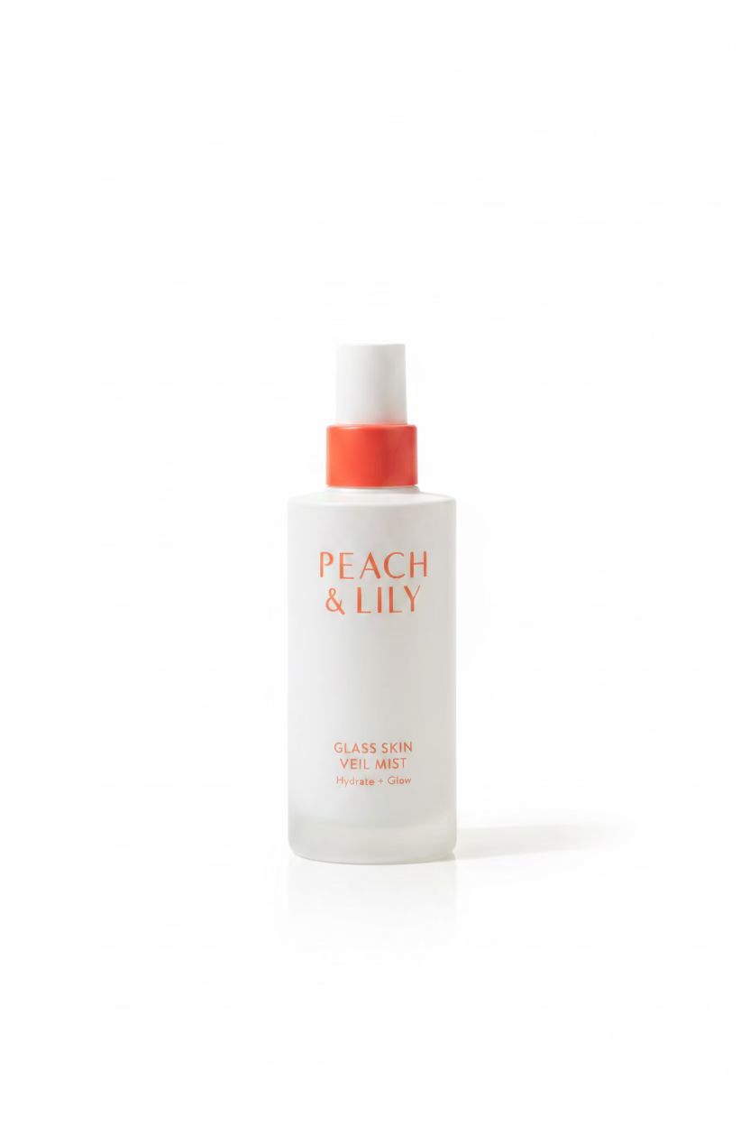 A white bottle of Peach & Lily Glass Skin Veil Mist with a coral-red pump cap, displayed on a glass shelf in front of Medcube skincare boxes.