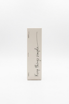 A tall, narrow beige cardboard box standing upright on a glass display counter inside a retail store. The box has black handwritten-style text reading 'Keep things simple' and a small circular logo near the top.