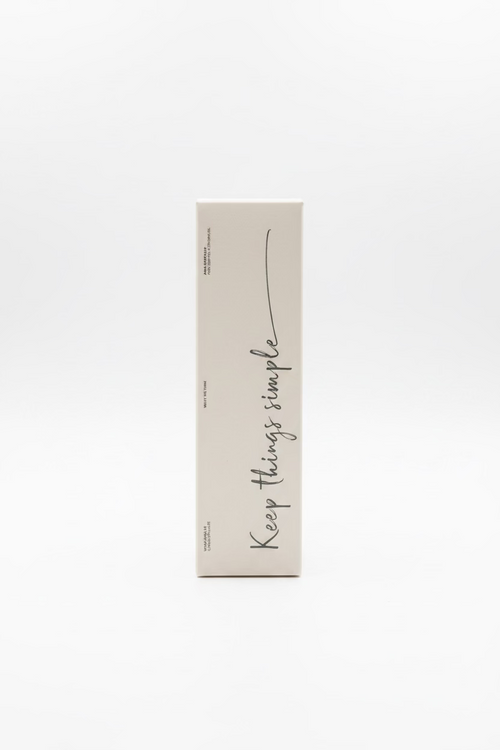 A tall, narrow beige cardboard box standing upright on a glass display counter inside a retail store. The box has black handwritten-style text reading 'Keep things simple' and a small circular logo near the top.