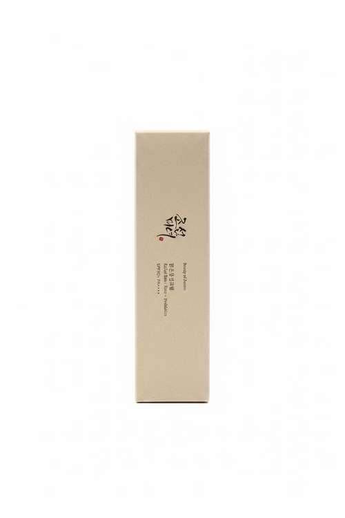 A tall, rectangular beige cosmetic box with black Korean text and a small red mark, standing upright on a glass display counter in a retail setting.