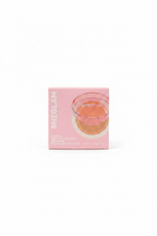 A pink box of SHEGLAM Gloworch Source Highlighter powder sits on a glass display shelf in a retail store. The packaging features a pink glow-in-the-dark glass cup illustration showing the product's effect.