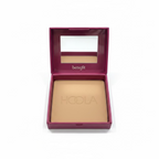 Benefit Hoola face powder in its magenta compact case, held in a hand. The compact lid features a mirror and the 'benefit' brand name, while the powder pan is embossed with 'HOOLA'.