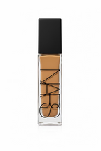 NARS liquid foundation in a clear rectangular bottle with a black cap, displayed on a glass counter in a retail setting.