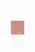 Two Hudabeauty matte powder compact boxes in a dusty pink color, displayed on a glass counter inside a retail store with shelves of other products in the background.
