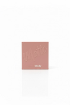 Two Hudabeauty matte powder compact boxes in a dusty pink color, displayed on a glass counter inside a retail store with shelves of other products in the background.
