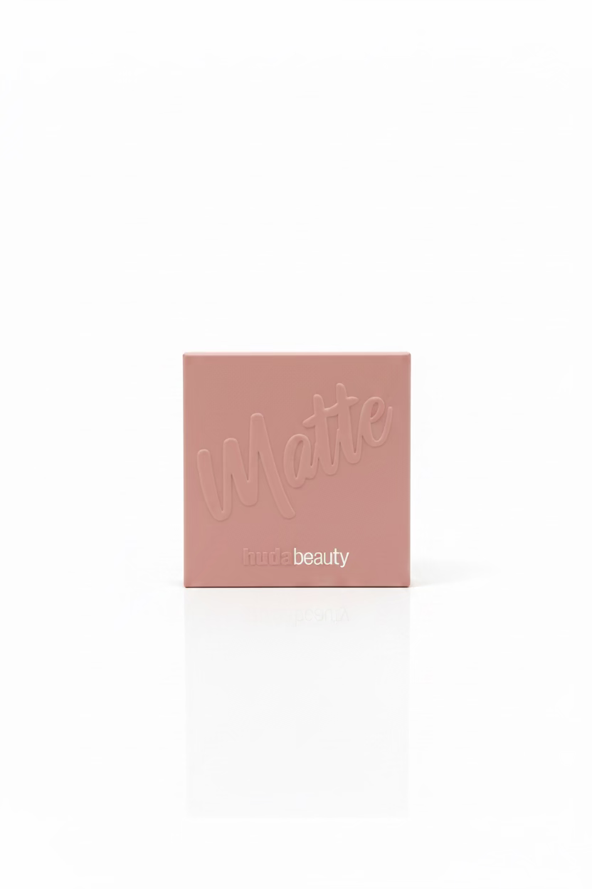 Two Hudabeauty matte powder compact boxes in a dusty pink color, displayed on a glass counter inside a retail store with shelves of other products in the background.
