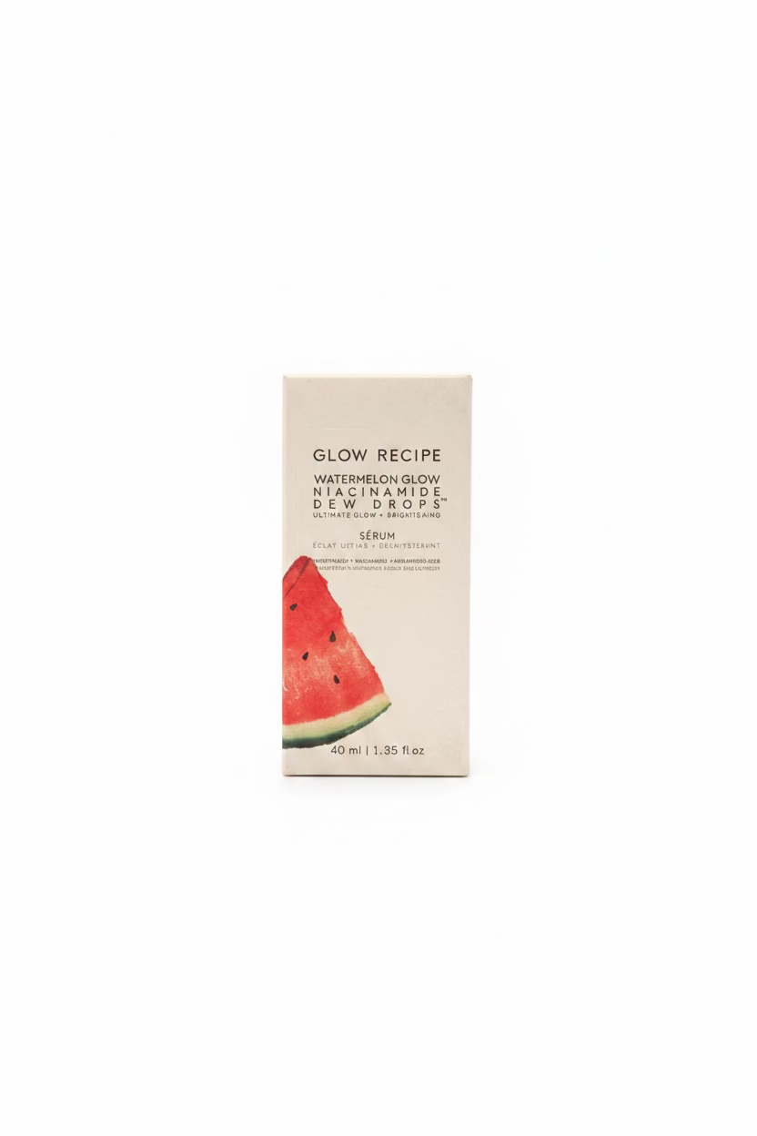 A box of Glow Recipe Watermelon Glow Macadamide Dew Drops stands on a counter in front of an open laptop, with shelves of skincare products in the background.