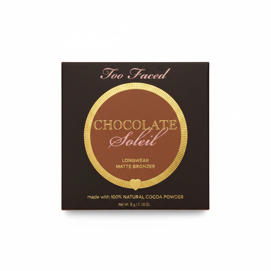 A box of Too Faced Chocolate Soleil Combed Matte Bronzer powder, placed on a glass table next to a laptop and a person's jeans.