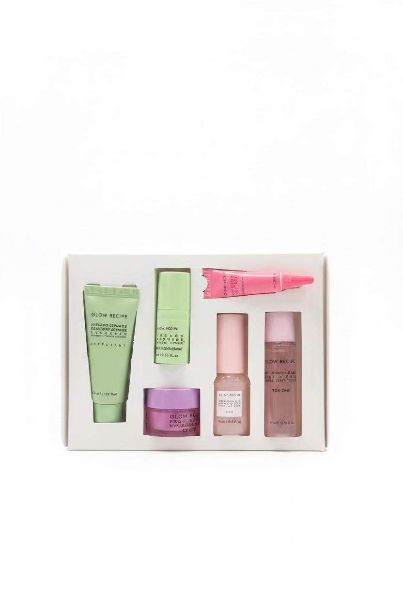 A boxed set of six cosmetic products arranged in a white tray, photographed on a glass display counter in a retail store. The set includes green, pink, and beige tubes and jars, with visible brand text including Glow Ron and Extrait de Beauté.