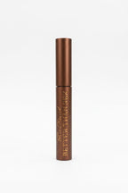 A brown cosmetic tube labeled 'BETTER THAN SEX' resting on top of its retail box in front of a glass display case.