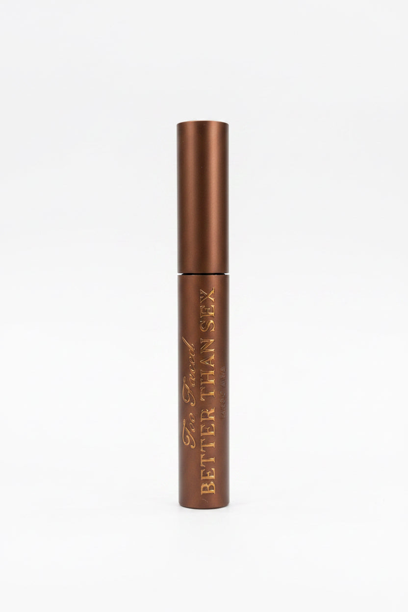 A brown cosmetic tube labeled 'BETTER THAN SEX' resting on top of its retail box in front of a glass display case.