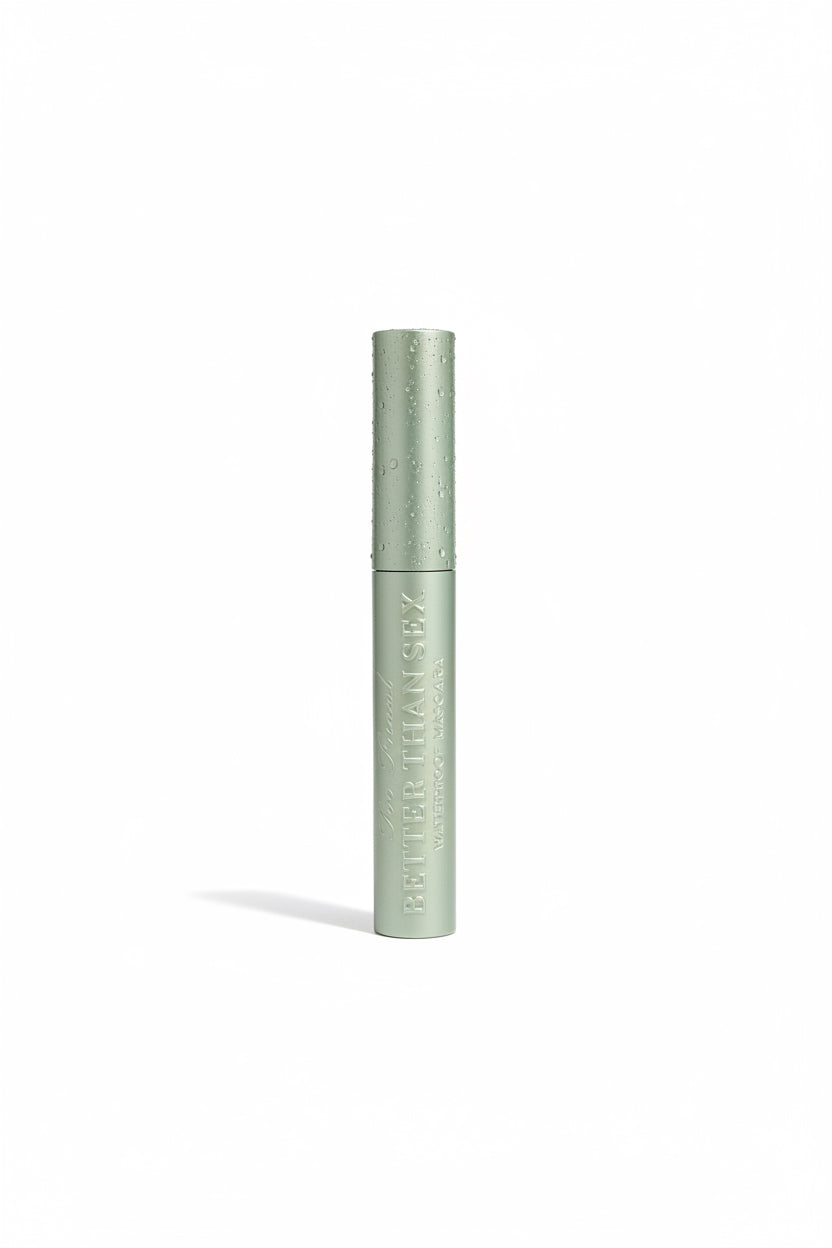 A close-up of a makeup pencil with a metallic olive green barrel and a dark gray tip, resting on top of an open laptop in a retail setting.