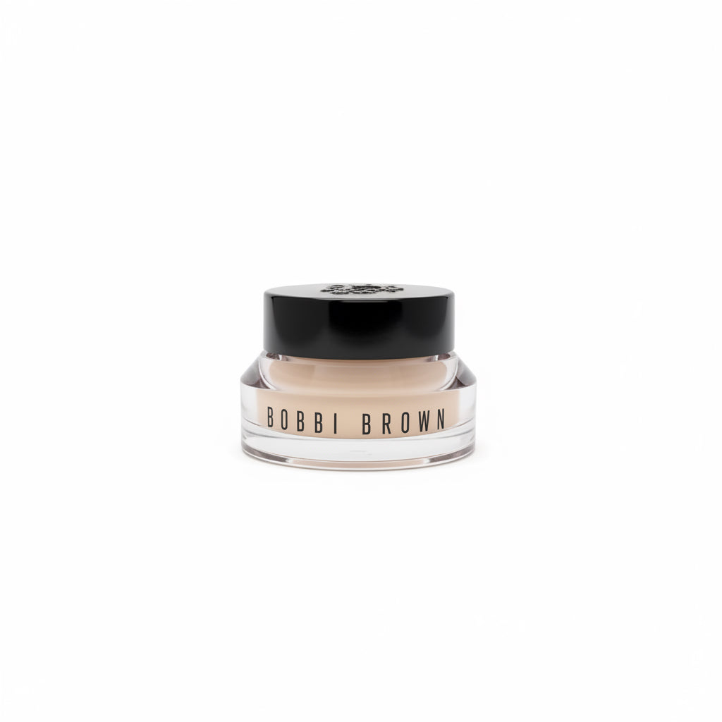 A jar of Bobbi Brown makeup sits on a silver laptop keyboard, with a red surface underneath and a blurred store or office background.
