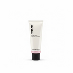 A squeeze tube of MAC Studio Cream in a white and black packaging with a pink band, displayed on a glass counter in a retail store with a laptop and shelves in the background.