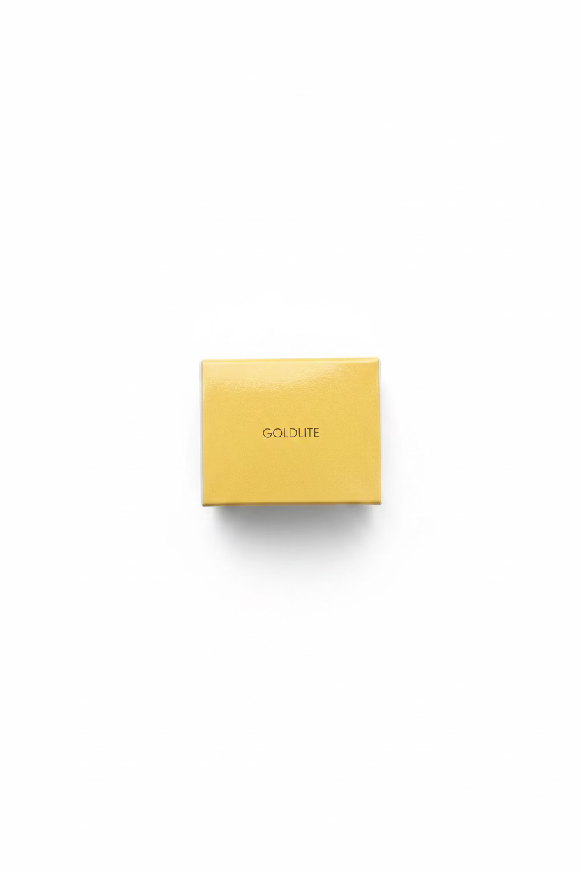 A hand holding a small yellow box labeled 'GOLDLITE' in a casual indoor setting with a person's legs and chair visible in the background.