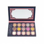 A makeup palette labeled 'TIMELESS TREASURES' held open in a store setting. The palette has 16 square pans in various glitter and matte shades of pink, gold, silver, and white, set against a dark background with pink ornate borders.