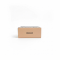 A beige cardboard box labeled 'MEDIUM' sits on a glass shelf in a retail setting, with a gold Mynk package below and a laptop and shelves in the background.