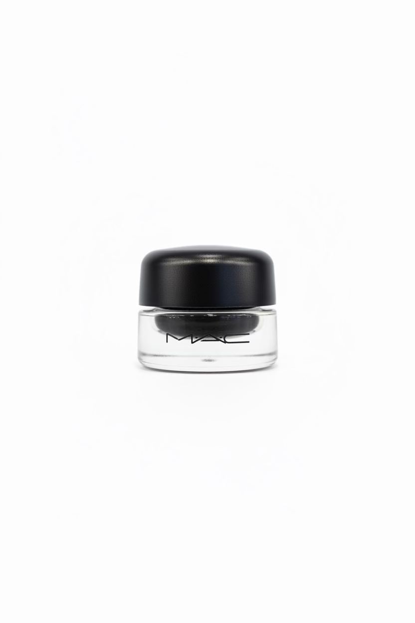 A hand holding a small clear jar of MAC Prime Color Glitter eyeshadow with a black lid, with a gold and green MAC product pouch blurred in the background.