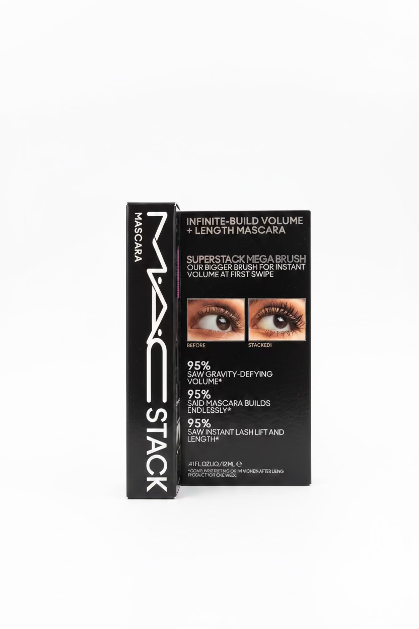 MAC Stack mascara box standing upright on a glass counter in a retail store. The black packaging shows the MAC logo, 'STACK' on the spine, and text for 'Infinite-Build Volume + Length Mascara' with before/after eye imagery and claims about the SuperStam Mega Brush.