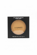 MAC Extra Dimension Skinfinish powder compact in its black retail box, displayed on a glass counter with a laptop and store shelves in the background.