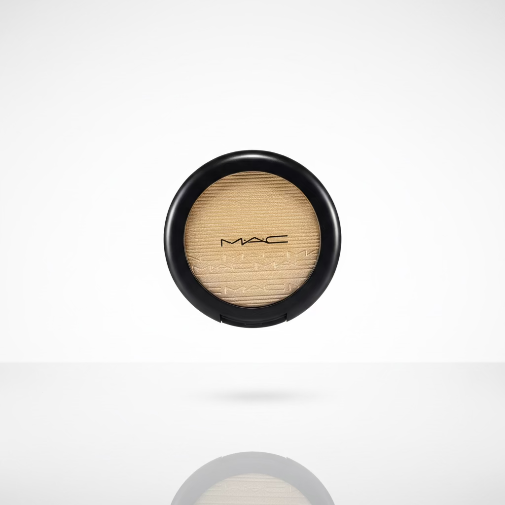 A hand holding a round black compact containing a shimmering gold eyeshadow, with a plastic-wrapped makeup item visible in the background.