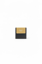 A hand holding a small black makeup compact or box with a beige label that reads 'BAKLAWA 346G'.