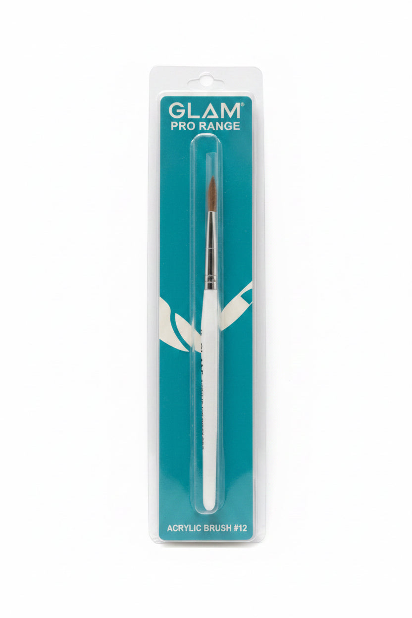 A packaged Glam Pro Range acrylic brush #12 standing upright in front of an open laptop on a desk. The brush is in clear plastic packaging with a teal card backing and a white handle visible through the package.