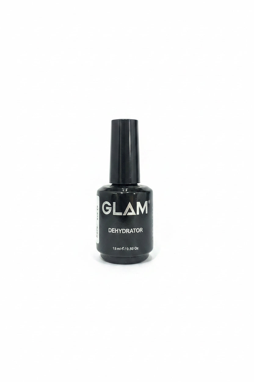 A hand holding a black bottle of GLAM Dehydrator nail polish against a background of blue jeans and a wooden cabinet.