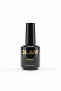 A black bottle of GLAM PRIMER 15 ml cosmetic product placed on top of an open silver laptop, with two more bottles in the background on a desk.