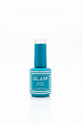 A bottle of GLAM No Wipe Top Coat nail polish in a teal blue shade, standing on a light gray tabletop with an open laptop in the background.